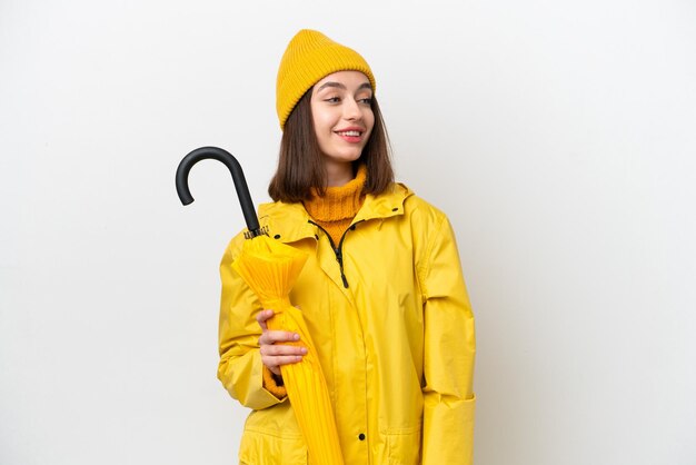 Photo jeune femme ukrainienne avec manteau imperméable et parapluie isolé sur fond blanc regardant sur le côté et souriant