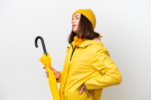 Jeune femme ukrainienne avec manteau imperméable et parapluie isolé sur fond blanc souffrant de maux de dos pour avoir fait un effort