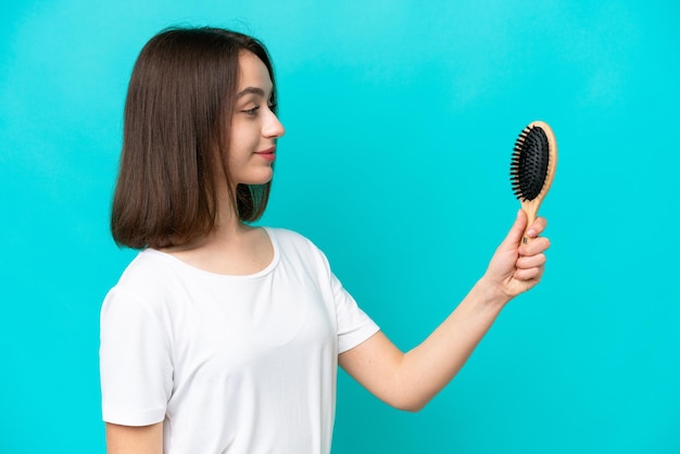 Jeune femme ukrainienne avec un peigne à cheveux isolé sur fond bleu avec une expression heureuse