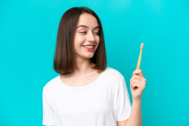 Jeune femme ukrainienne se brosser les dents isolé sur fond bleu avec une expression heureuse