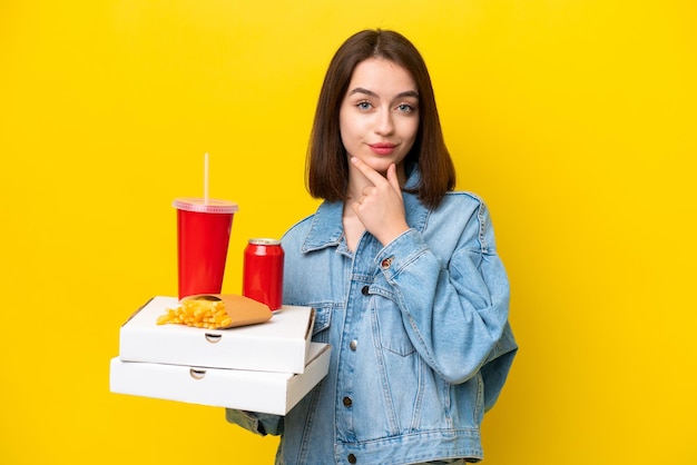 Jeune femme ukrainienne tenant une restauration rapide isolée sur fond jaune pensant