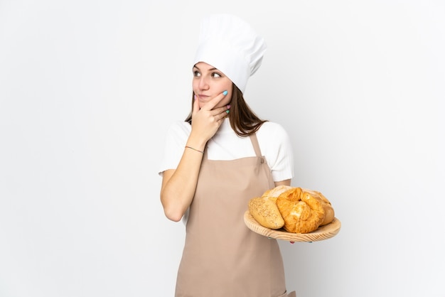 Jeune femme en uniforme de chef sur mur blanc en pensant à une idée