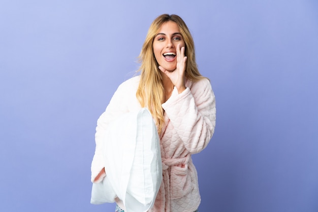 Jeune femme uruguayenne blonde isolée sur bleu en pyjama et criant avec la bouche grande ouverte