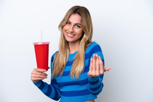 Jeune femme uruguayenne buvant du soda isolé sur fond blanc invitant à venir avec la main Heureux que vous soyez venu