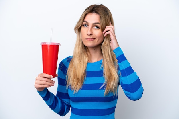 Jeune femme uruguayenne buvant du soda isolé sur fond blanc en pensant à une idée