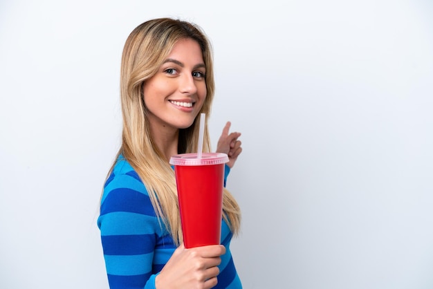 Jeune femme uruguayenne buvant du soda isolé sur fond blanc pointant vers l'arrière