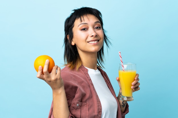 Jeune femme uruguayenne sur fond bleu isolé tenant une orange et un jus d'orange