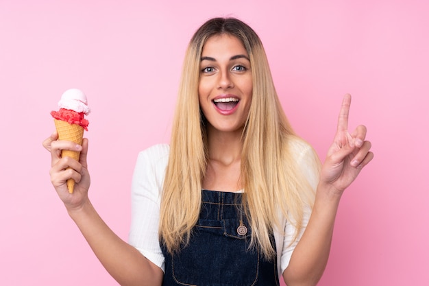 Jeune femme uruguayenne avec une glace au cornet sur mur isolé mur rose pointant vers le haut une excellente idée