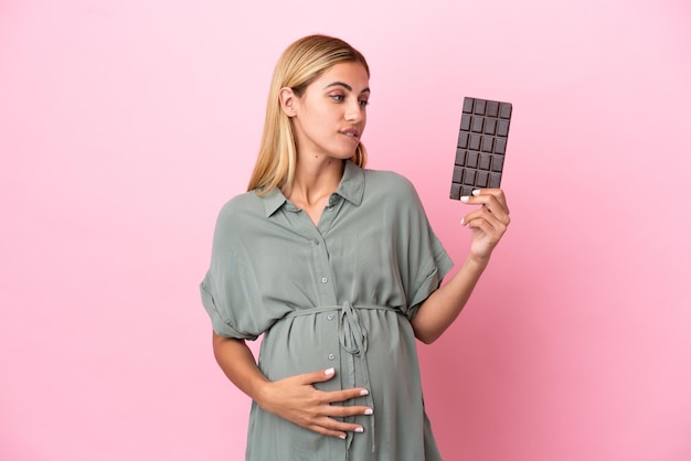 Jeune femme uruguayenne isolée sur fond bleu enceinte et tenant du chocolat avec faim