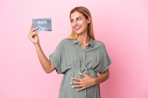 Jeune femme uruguayenne isolée sur fond bleu enceinte et tenant une échographie