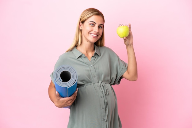 Jeune femme uruguayenne isolée sur fond bleu enceinte tenant une pomme et allant à des cours de yoga