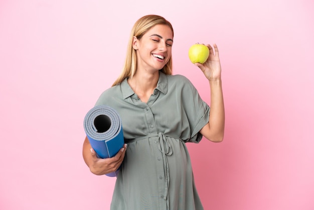 Jeune femme uruguayenne isolée sur fond bleu enceinte tenant une pomme et allant à des cours de yoga