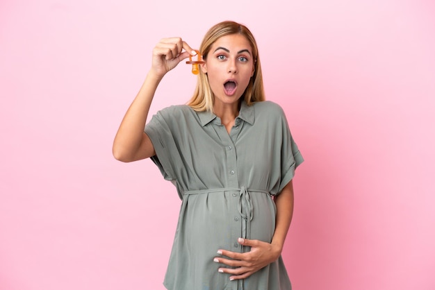 Jeune femme uruguayenne isolée sur fond bleu enceinte et tenant une tétine avec une expression surprise