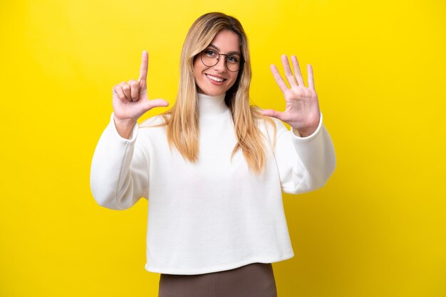 Jeune femme uruguayenne isolée sur fond jaune comptant sept avec les doigts