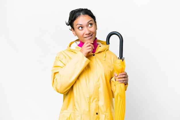 Jeune femme uruguayenne avec manteau imperméable et parapluie sur fond blanc isolé et levant les yeux