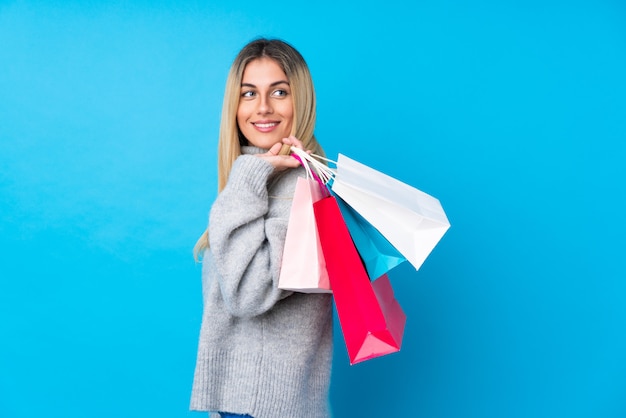 Jeune femme uruguayenne sur mur bleu isolé tenant des sacs à provisions et souriant