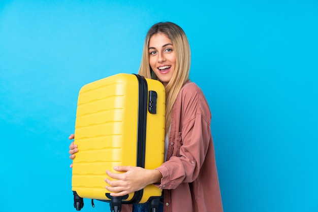 Jeune femme uruguayenne sur mur bleu isolé en vacances avec valise de voyage et surpris