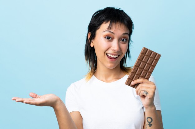 Jeune femme uruguayenne sur mur bleu en prenant une tablette de chocolat et surpris