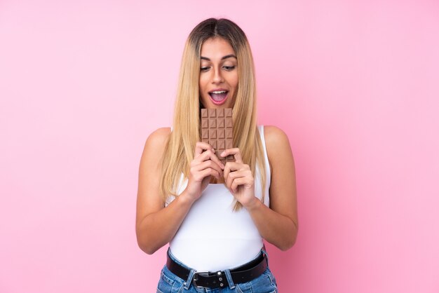 Jeune femme uruguayenne sur mur isolé mur rose manger une tablette de chocolat