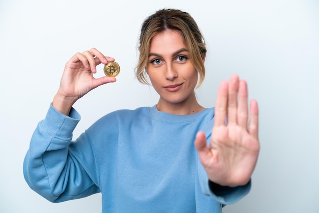 Jeune femme uruguayenne tenant un bitcoin isolé sur fond blanc faisant un geste d'arrêt