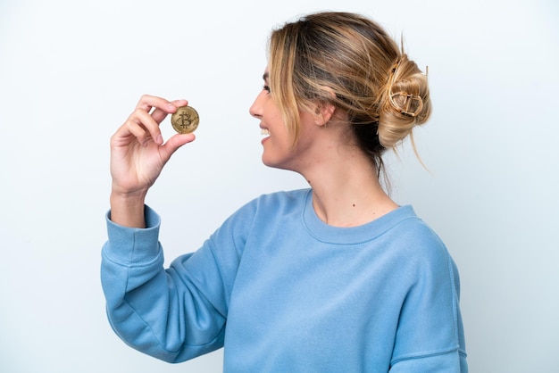 Jeune femme uruguayenne tenant un Bitcoin isolé sur fond blanc rire en position latérale