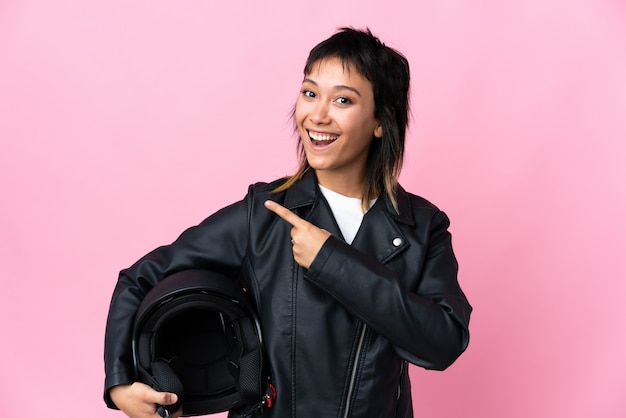 Jeune femme uruguayenne tenant un casque de moto sur fond rose isolé pointant le doigt sur le côté