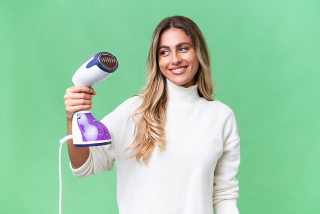 Jeune femme uruguayenne tenant un fer à repasser sur fond isolé avec une expression heureuse