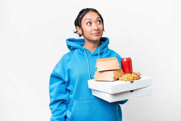 Jeune femme uruguayenne tenant des pizzas et des hamburgers sur fond blanc isolé et levant les yeux