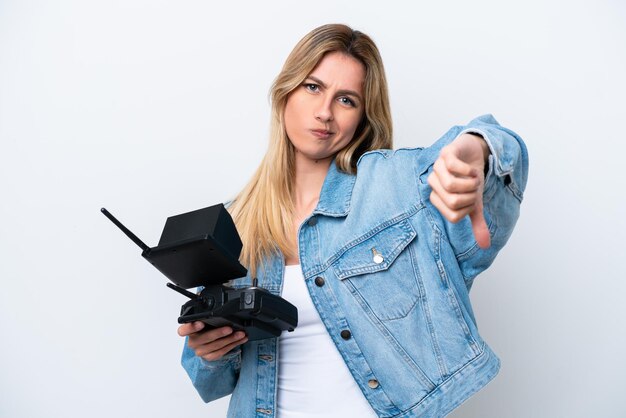 Jeune femme uruguayenne tenant une télécommande de drone isolée sur fond blanc montrant le pouce vers le bas avec une expression négative