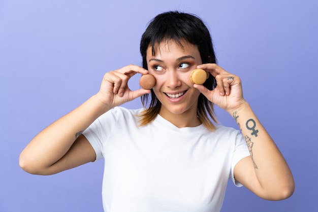 Jeune femme uruguayenne sur violet isolé tenant des macarons français colorés et levant