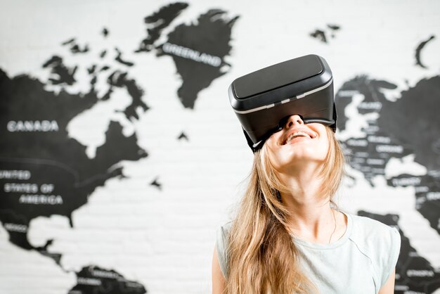 Jeune femme utilisant des lunettes de réalité virtuelle assise à l'intérieur avec une carte du monde en arrière-plan