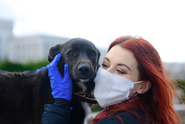 Jeune femme utilisant un masque facial comme prévention contre la propagation du coronavirus en marchant avec son chien. Image de concept de pandémie mondiale COVID-19.