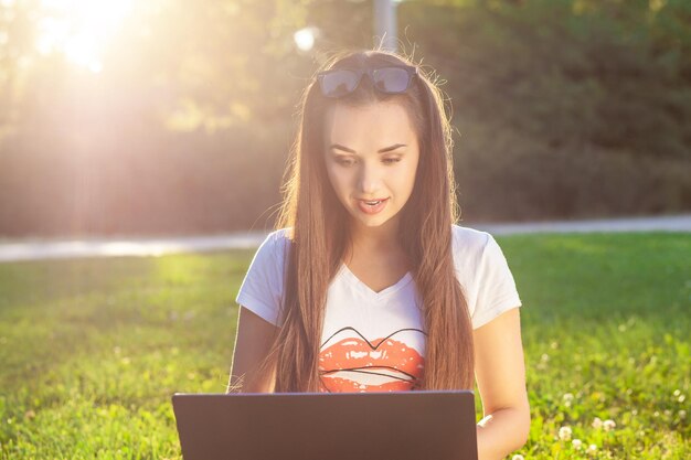 Jeune femme utilisant un ordinateur sur des herbes vertes dans l'apprentissage de l'éducation du parc ou travaillant à la pige ...