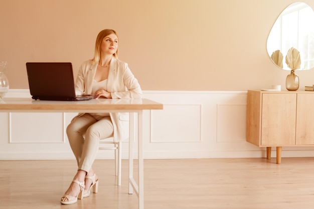 Jeune femme utilisant un ordinateur portable au bureau à domicile assis sur la table et regardant vers la fenêtre