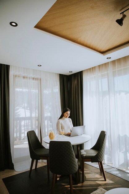 Jeune femme utilisant un ordinateur portable et buvant du jus d'orange sain dans la chambre