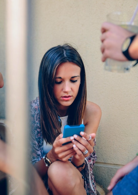 Une jeune femme utilisant un téléphone portable alors qu'elle est assise contre le mur