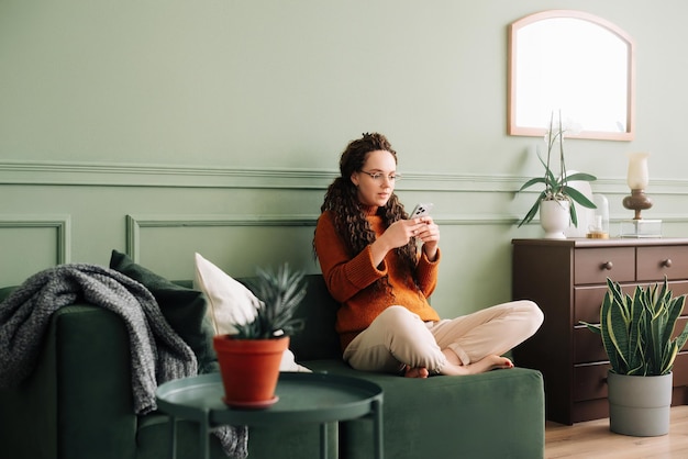 Jeune femme utilisant un téléphone portable assise sur le canapé à la maison