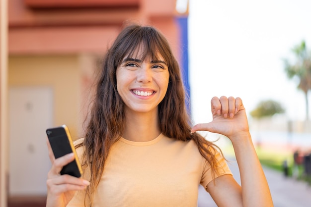 Jeune femme utilisant un téléphone portable à l'extérieur fière et satisfaite