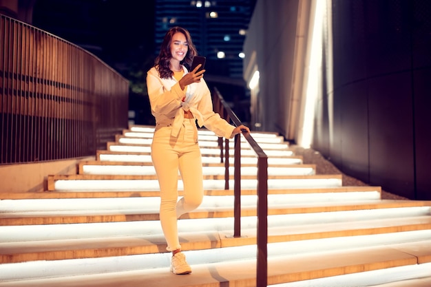 Jeune femme utilisant un téléphone portable pendant une promenade dans la ville nocturne en descendant la copie des escaliers illuminés