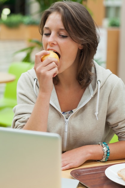 Jeune femme, utilisation, ordinateur portable, quoique, manger, pomme