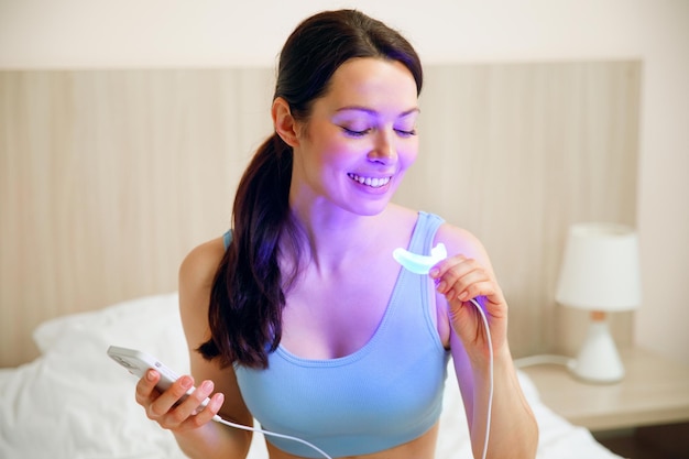 Une jeune femme utilise un complexe de blanchiment pour le blanchiment des dents à domicile lampe uv usb pour le blanchiment des dents