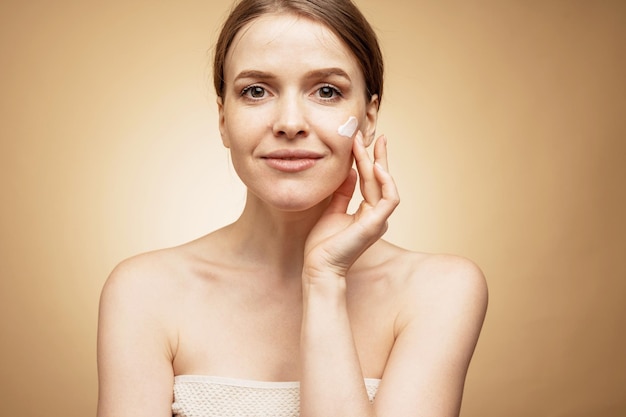 Une jeune femme utilise une crème et un exfoliant pour le visage pour hydrater la peau