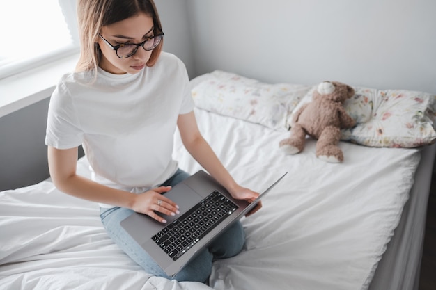 Jeune femme utilise un ordinateur portable à la maison sur le lit