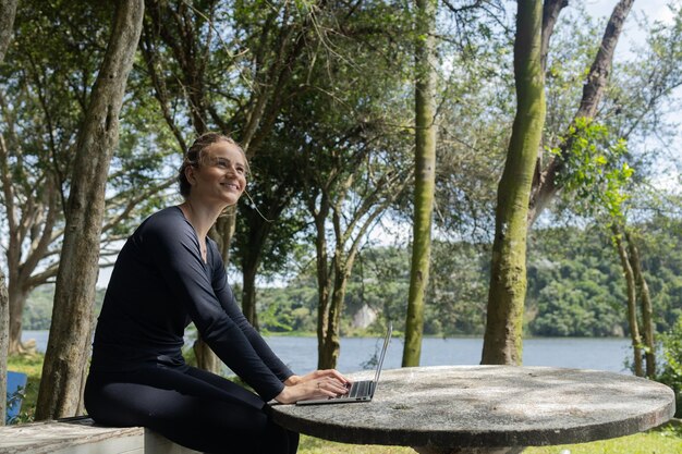 Une jeune femme utilise un ordinateur portable pendant la journée dans un parc vert.