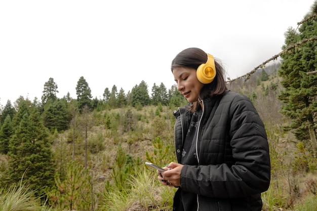 Une jeune femme utilise ses écouteurs pour écouter de la musique en se promenant dans la forêt par un après-midi nuageux