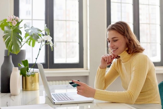 Une jeune femme utilise son téléphone alors qu'elle est assise sur la table à la maison.