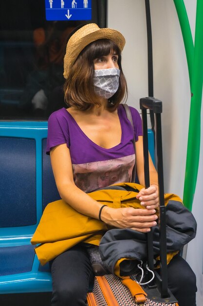 Une jeune femme avec une valise et un chapeau assis attendant le métro