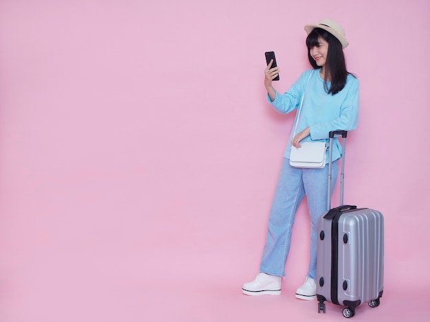 Jeune femme avec valise et smartphone sur mur rose