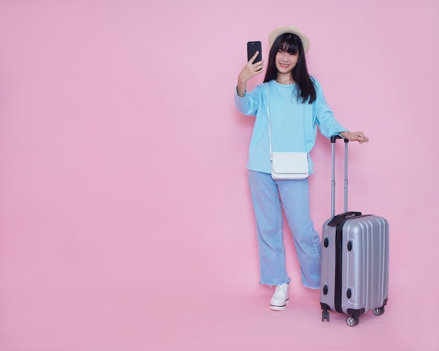 Jeune femme avec valise et smartphone sur mur rose