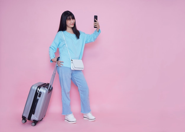 Jeune femme avec valise et smartphone sur mur rose